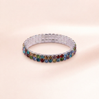 A silver-toned stretch bracelet featuring two rows of colorful square rhinestones in shades of blue, green, red, and gold, displayed on a soft pink background.