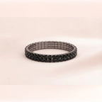 A black magnetic stretch bracelet with a textured, star-like pattern on the front, displayed on a soft beige background.