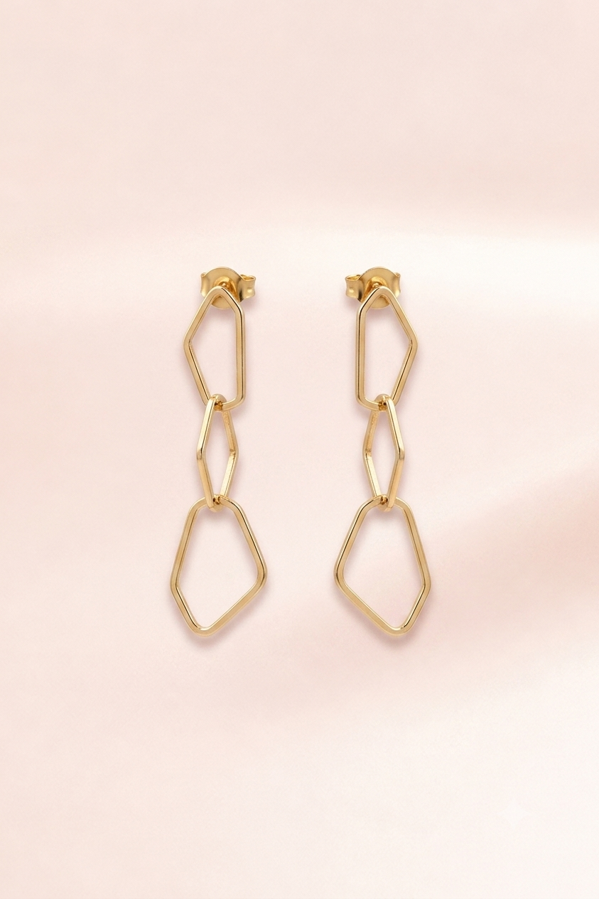 A pair of gold geometric drop earrings with a double-link chain design, displayed on a soft, light pink background.