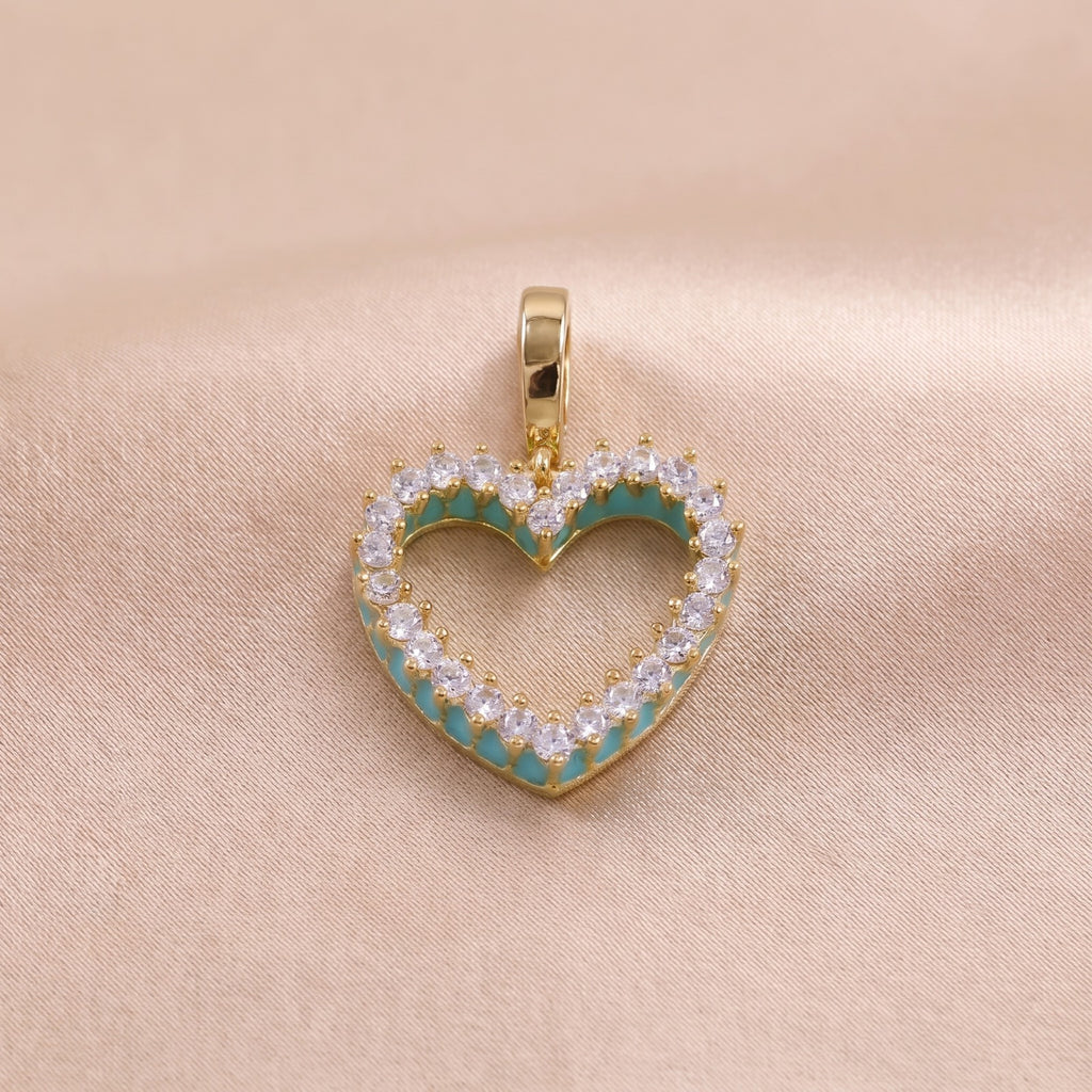 A gold heart-shaped pendant charm with a turquoise enamel inlay and clear round-cut stones, shown on a soft pink background.