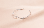 A silver-toned open cuff bracelet with three small white pearls, displayed on a soft beige fabric background.