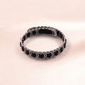 A silver-toned chain-link bracelet with alternating black oval links, displayed on a soft, light beige background.