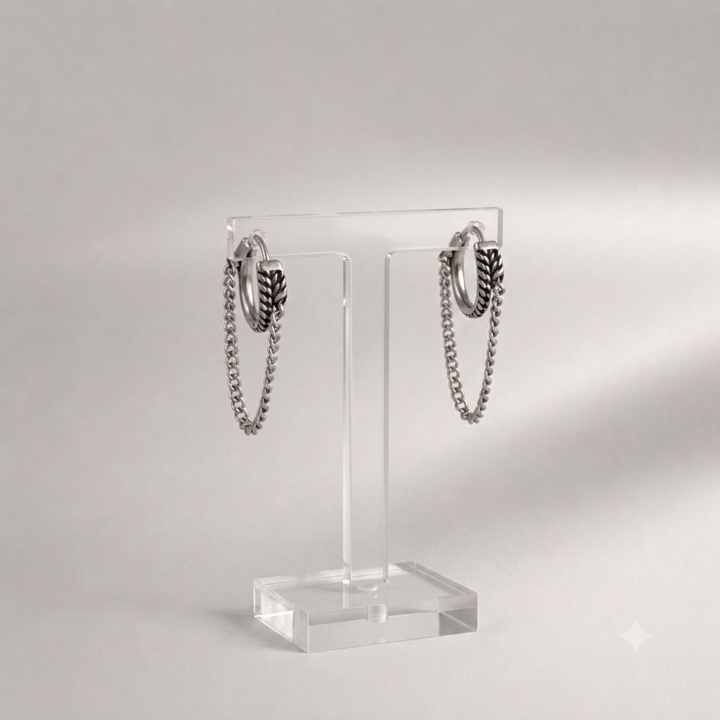 A pair of silver-toned hoop earrings with hanging chain and feather-like dangle details, displayed on a clear acrylic stand against a soft light gray background.