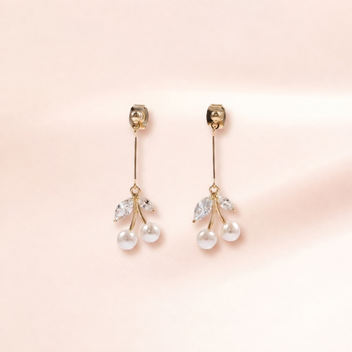 A pair of gold dangle earrings with clear marquise-cut crystals and two white pearl drops, displayed on a soft pink background.