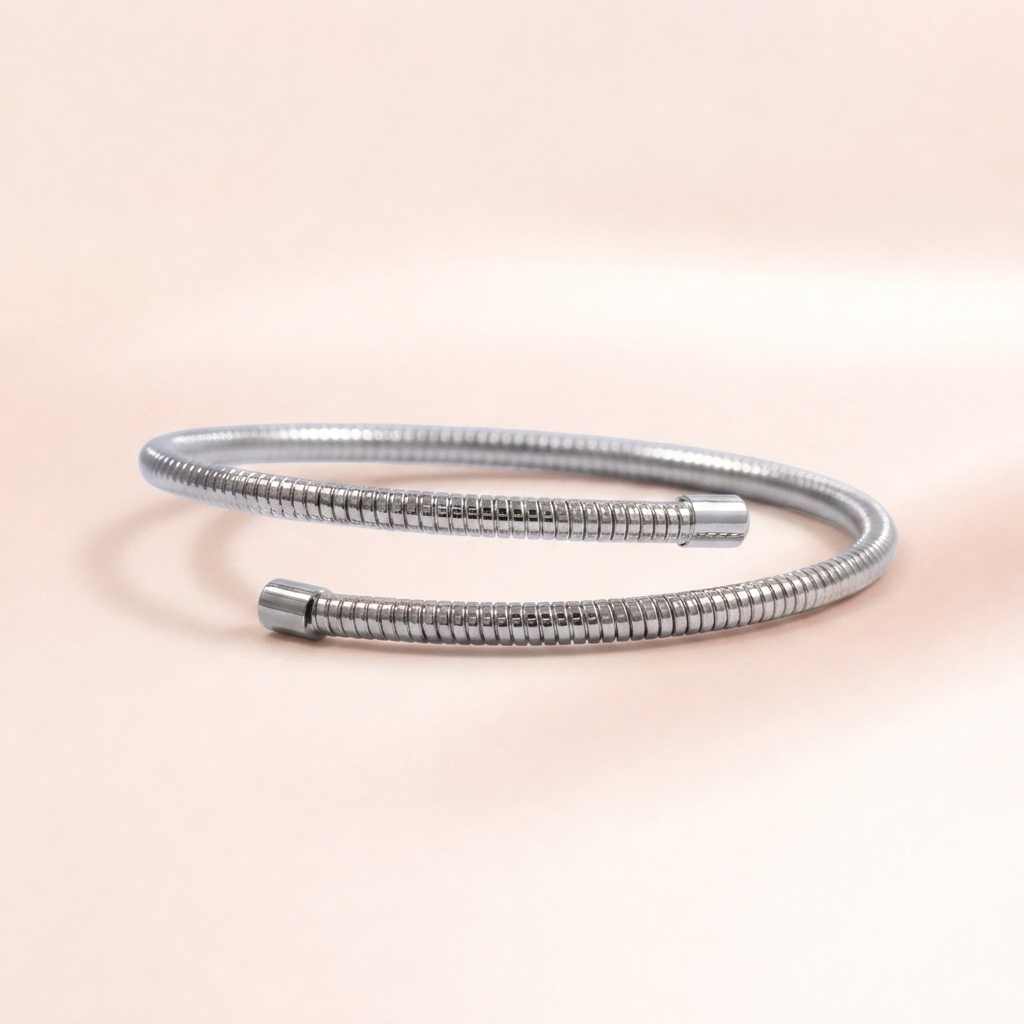 A silver metallic snake-style bangle bracelet with a textured, ribbed outer surface and smooth cylindrical end caps, photographed on a soft peach-pink background.