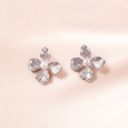 A pair of silver flower-shaped stud earrings with textured petals and a small white pearl in the center, displayed on a soft, light pink background.
