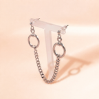 A pair of silver-toned chain hoop earrings displayed on a translucent T-stand against a warm peach background.