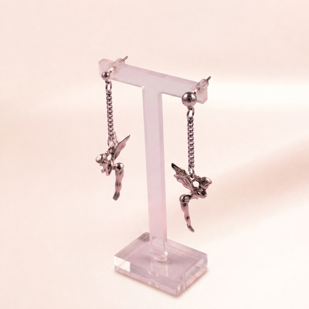 A pair of dangling fairy earrings in a dark metallic finish, displayed on a translucent pink acrylic T-stand against a soft, pale pink background.