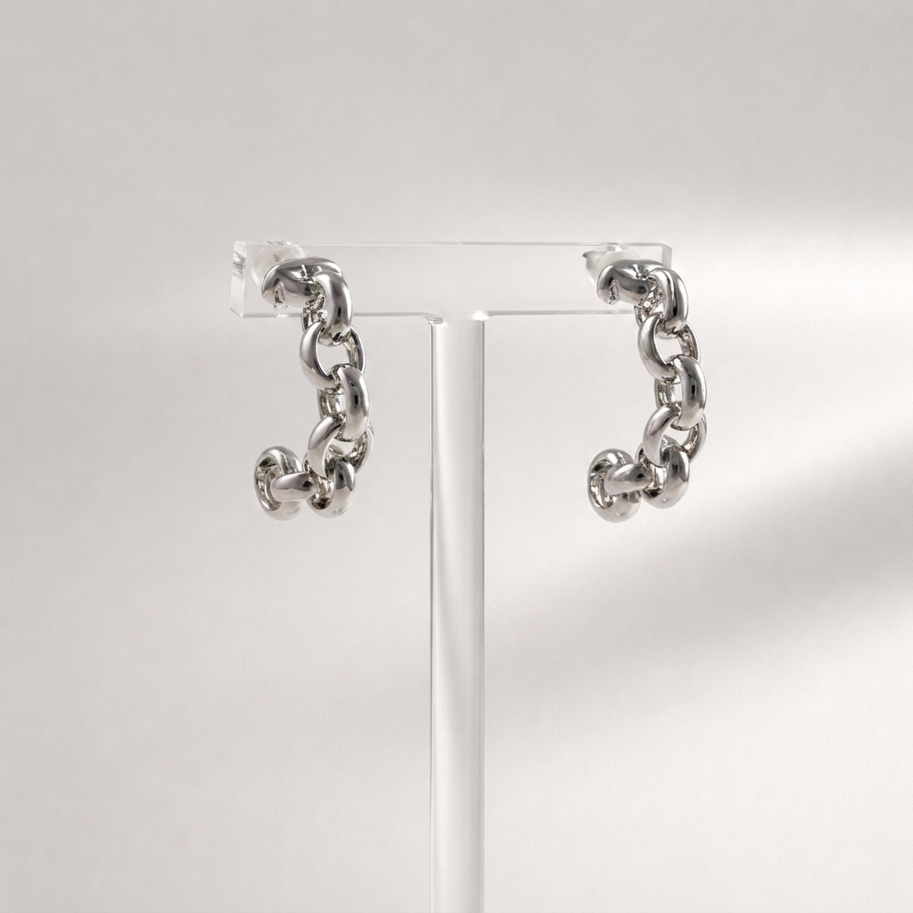 A pair of chunky silver chain hoop earrings displayed on a clear acrylic stand against a light gray background.