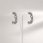 A pair of chunky silver chain hoop earrings displayed on a clear acrylic stand against a light gray background.