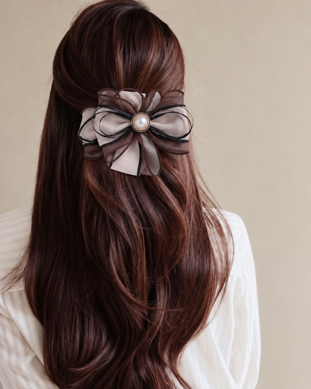A long, wavy dark brown hair accessory with a large bow made of taupe and black sheer ribbon, featuring a central pearl-like embellishment, shown pinned to a model's half-up hairstyle.